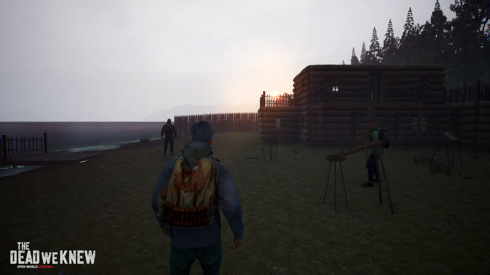 Official THE DEAD WE KNEW screenshot showing survivors beside a lakeside log shelter